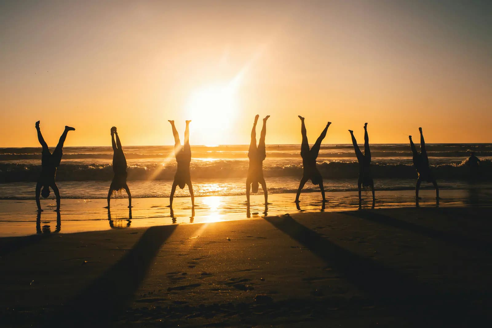 A group practising yoga on a beach at sunset